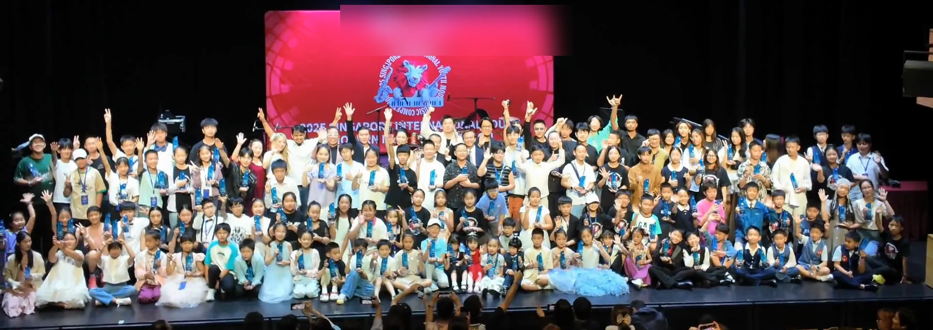Hundreds of young participants gathered across a stage, waving and celebrating together