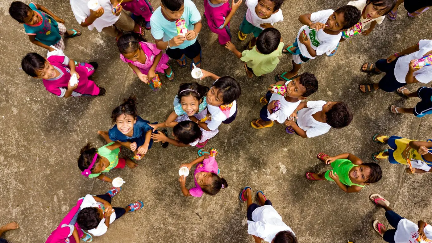A large group of children in colourful clothes gathered in circles, seen from above
