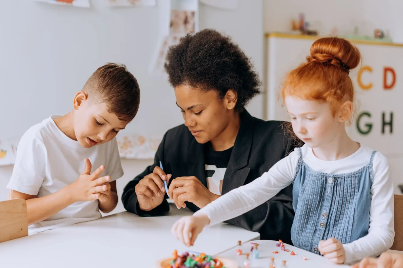 An educator guiding two young children through a hands-on activity at a table